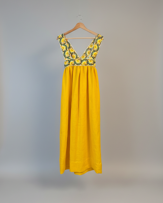 Yellow dress with floral top on a hanger against a white wall.