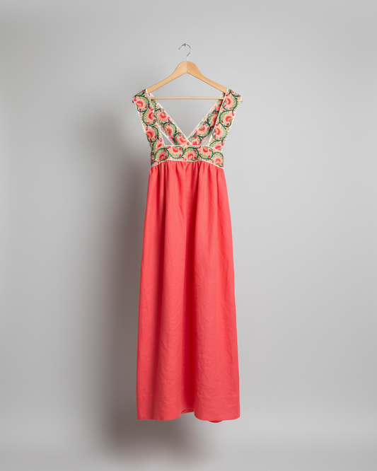 Red dress with floral embroidery on a hanger against a white wall.