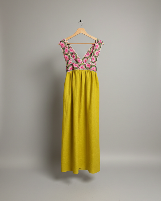 Yellow dress with floral top on a hanger against a white wall.