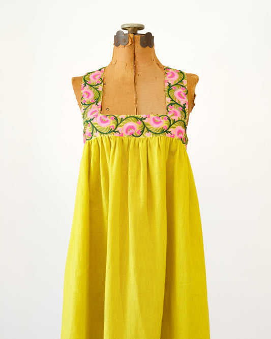 A bright yellow linen nightgown with a floral embroidered bodice, displayed on a vintage wooden dress form against a white background.