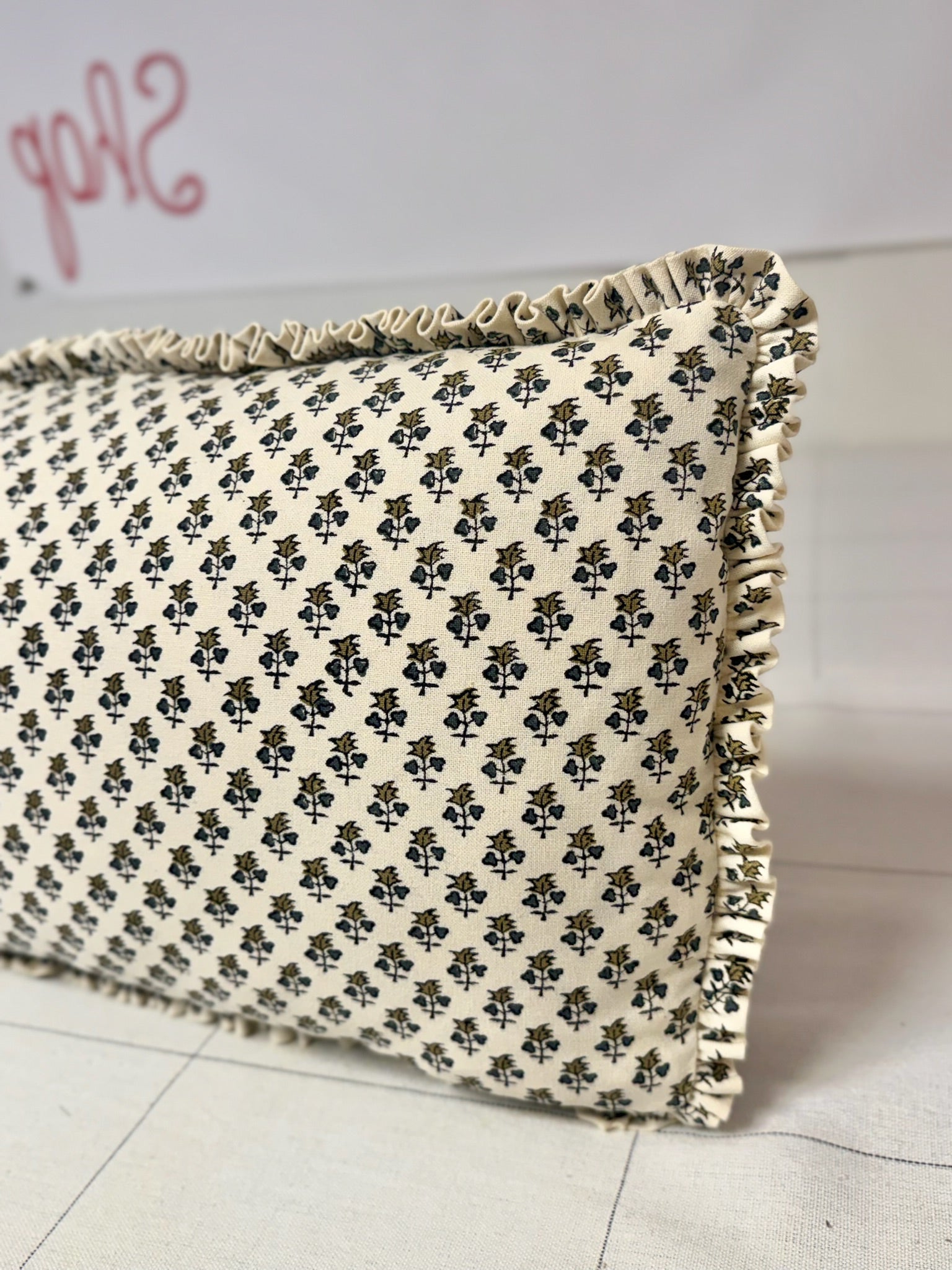 A close-up of a rectangular throw pillow with a black and cream floral block print and ruffled trim, resting on a light-colored floor.