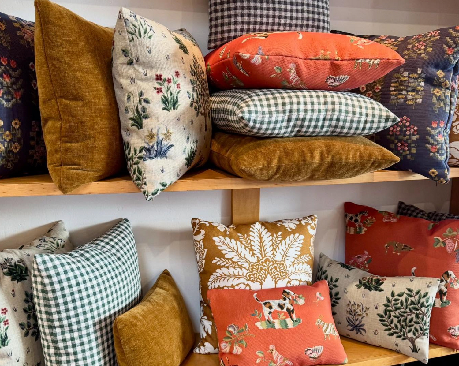 A collection of decorative throw pillows in various colors and patterns, including gingham, floral, and textured fabrics, displayed on wooden shelves.